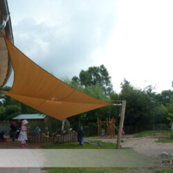 Rollbares Sonnensegel in Waldorfkindergarten Manuell aufrollbares Sonnensegel an einem Holzhaus und an Robinienpfosten in einem Waldorfkindergarten