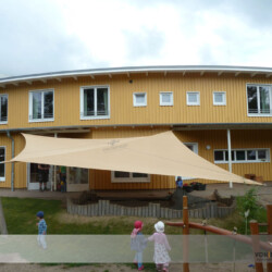 Rollup-Segel in Naturkindergarten Manuell aufrollbares Sonnensegel an einem Holzhaus und an Robinienpfosten in einem Waldorfkindergarten