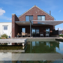 Sonnenschutz beim Relaxen und Baden Aufrollbares Sonnensegel auf der Terrasse eines Wohnhauses mit Schwimmteich in Buxtehude