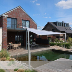 Textile Architektur - motorisch aufrollbar Aufrollbares Sonnensegel auf der Terrasse eines Wohnhauses mit Schwimmteich in Buxtehude