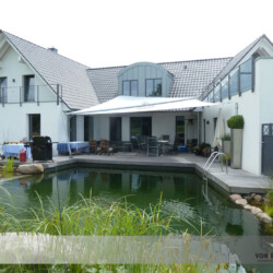 Schwimmteich mit aufrollbarem Sonnensegel Blick über einen Schwimmteich auf ein Soliday-Sonnensegel an einem luxuriösen Haus nähe Kiel