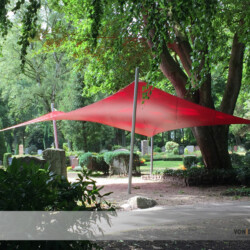 Freundlicher Farbfleck auf einem Friedhof Das rote Sonnen- und Wetterschutzsegel bietet Schutz für Trauergäste